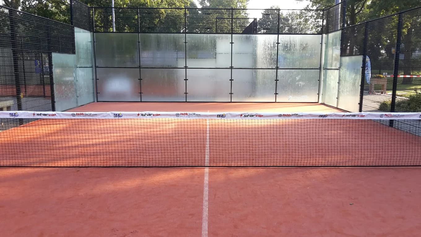 Outdoor padel court met rode ondergrond, omsloten door glazen en metalen mesh wanden.