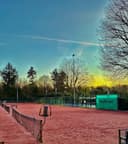 Padelclub met rode banen bij zonsondergang, verlicht en omgeven door bomen