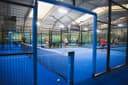 Overdekte padelclub met blauwe QuickPadel-banen, spelers in actie, professionele verlichting
