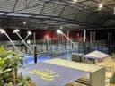 Moderne indoor padelclub met blauwe QuickPadel-banen, verlicht en voorzien van zithoek