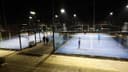 Outdoor padeltennisbanen met blauwe hard court oppervlak, omgeven door glas en gaas, verlicht 's nachts.