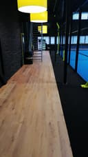Binnen padelbaan met gele verlichting, houten vloer en blauwe wanden