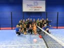 Groepsportret op blauwe padelbaan met netwerk omheining en academy signage.