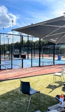 Outdoor padelclub met afgesloten courts, blauwe kunstgrasoppervlak, zwarte mesh-omheining en schaduwdoeken.