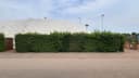 Buitenpadelclub met witte afdekking, groene heg en verlichting