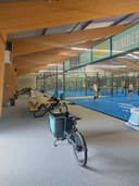 Binnenpadelclub met blauwe velden, fietsen en houten plafond met verlichting