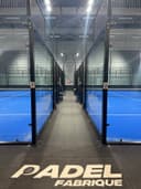 Padel Fabrique binnenhallen met twee blauwe courts, zwarte glaswanden en professionele verlichting