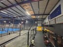 Moderne overdekte padelbanen met blauwe ondergrond, verlicht, zitplaatsen en gele deur zichtbaar.