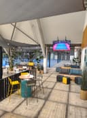 Moderne padelbaan met lounge, gele stoelen en TV-scherm, blauwe binnenbaan zichtbaar