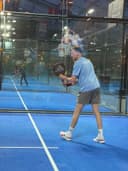 Padelspeler in blauw shirt speelt op indoor padelbaan met blauwe hardcourt