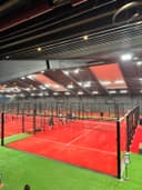 Overdekte padelbaan met rood speelveld, kunstgras zijvelden en moderne LED-verlichting.