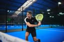 Padelspeler in actie op blauwe indoorbaan met gele racket in modern sportcomplex