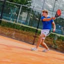 Jonge tennisser speelt op oranje padelbaan met netwerk op achtergrond