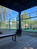 Moderne padelbanen buiten met glazen wanden en groene kunstgrasveld onder blauwe hemel