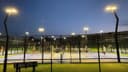 Verlichte padelbanen 's avonds met groene kunstgrasvelden en volledig gaasomheiningen