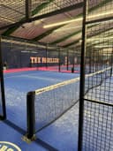 Overdekt padelcourt met blauwe QuickPadel ondergrond, omsloten door mesh wanden en glas achterwand bij The Padellers.