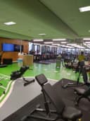 Moderne indoorpadelbaan met groen kunstgrasveld, glazen wanden, zwarte apparatuur en receptie.