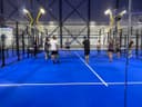 Binnenpadelbaan met blauwe hardcourt, spelers in training onder LED-verlichting