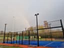 Outdoor padelbaan met blauwe QuickPadel ondergrond en zwarte omheining, floodlights zichtbaar