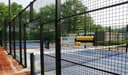 Outdoor padelbanencomplex met blauwe hardcourts, zwarte omheining en gele ballenhouders