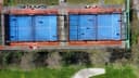 Luchtfoto van twee padelbanen met blauwe hardcourt en rode omheining naast elkaar