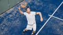 Padelspeler in witte outfit serveren op blauwe outdoor padelcourt