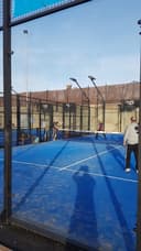 Buitenpadelbaancomplex met blauwe QuickPadel-courts, verlicht door floodlights, omgeven door netting en hekwerk.
