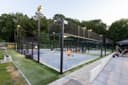 Moderne openlucht padelclub met verlichte courts, glazen en mesh omheining, blauwe hardcourts en spectatorplaatsen.